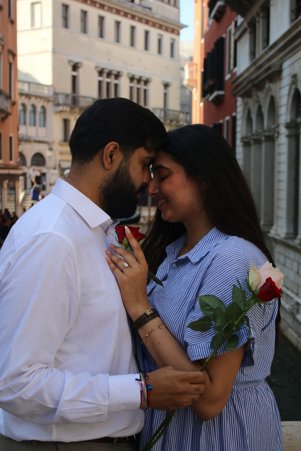 Milan and Gurleen touching foreheads, holding roses in Venice after their proposal